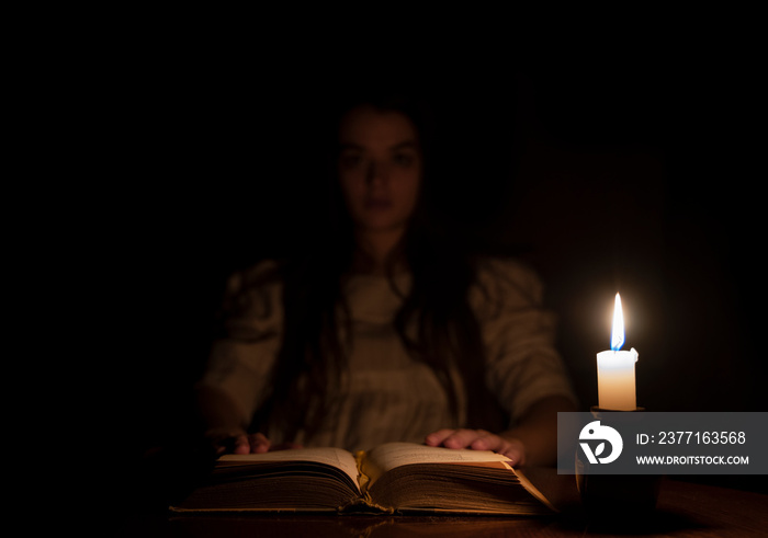 A young girl holding a book at night in candle light. She is wearing an old white dress.  The focus 