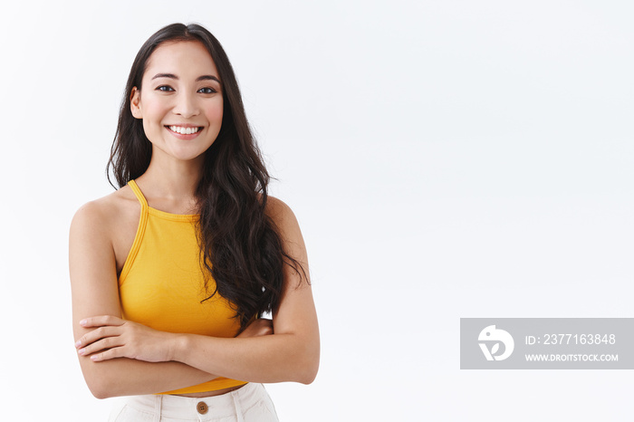 Confident, attractive young outgoing asian woman in yellow top, smiling friendly and happy as cross 