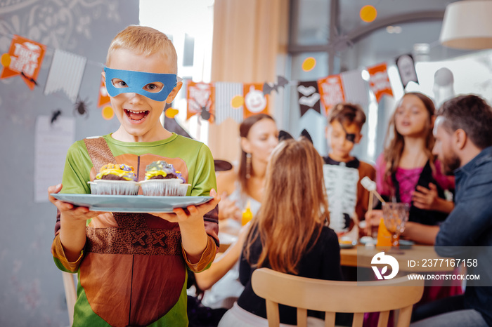 Ninja turtle. Blonde-haired schoolboy wearing Ninja turtle costume for Halloween looking extremely h