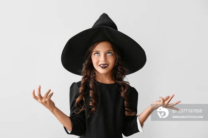 Cute little girl dressed as witch for Halloween on light background