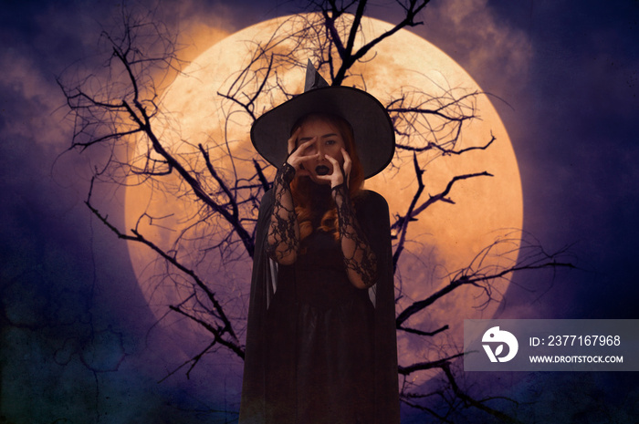 Scary halloween witch standing over dead tree, full moon and spooky cloudy sky, Halloween mystery co