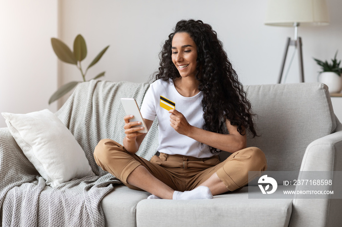 Happy woman using mobile phone and credit card at home