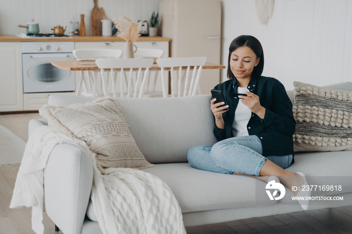 Client is purchasing online from home on quarantine. Young woman holding smartphone and credit card.