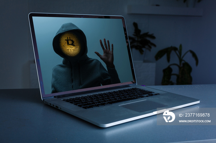 Man without a face in a hood holds a luminous bitcoin icon on a dark background.