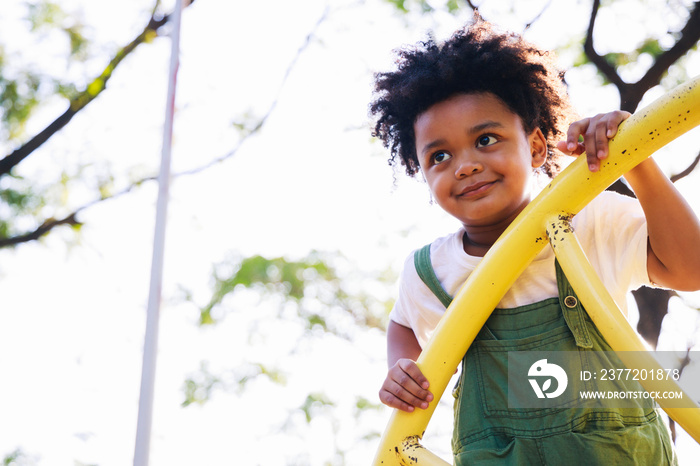 Cute African American little kid boy having fun while playing on the playground in the daytime in su