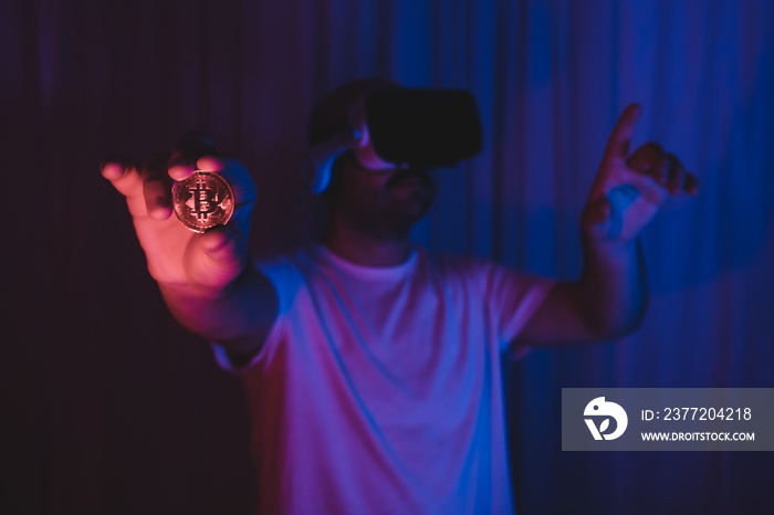 Young man entering the virtual world with bitcoin. man in vr glasses is holding btc coin in his hand