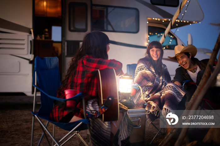 Smiling friends sitting by motorhome at dusk