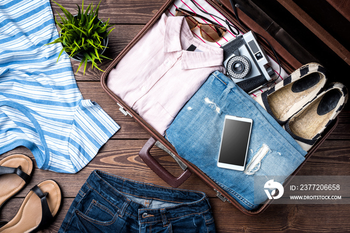 Open suitcase with casual female clothes on wooden table