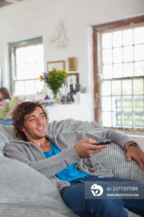 Young man with remote control watching TV in beanbag chair