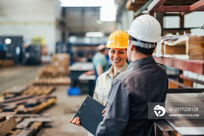 Two positive colleagues talking in heavy industry factory.