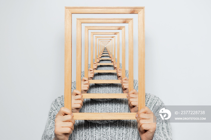 Enigmatic surrealistic optical illusion, young man holding frame on grey background.