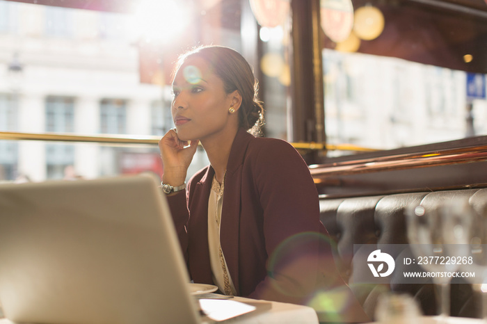 Serious businesswoman with laptop working in sunny restaurant