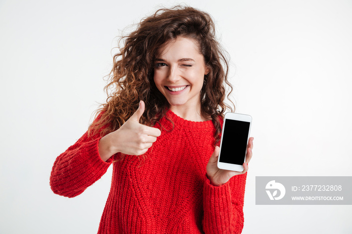 Smiling woman showing blank smartphone screen and thumb up