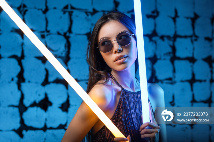 Toned portrait of beautiful woman with neon lamps on dark color background