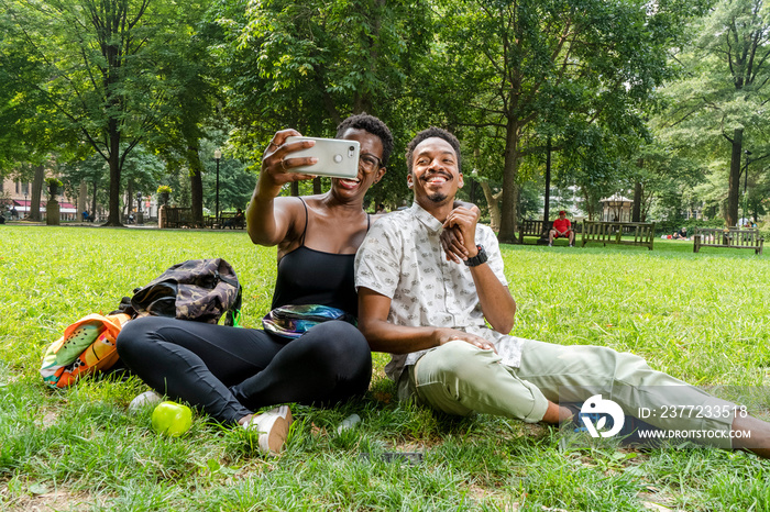 Smiling couple taking�selfie�on lawn in park