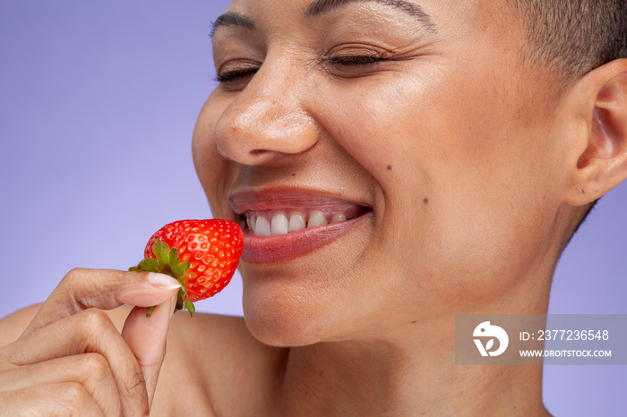 Close-up of smiling woman holding strawberry against purple background