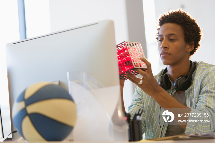 Creative young businessman examining prototype at computer in office