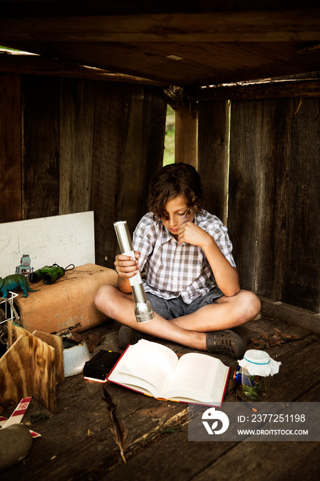 Boy reading book in wooden shed using torch