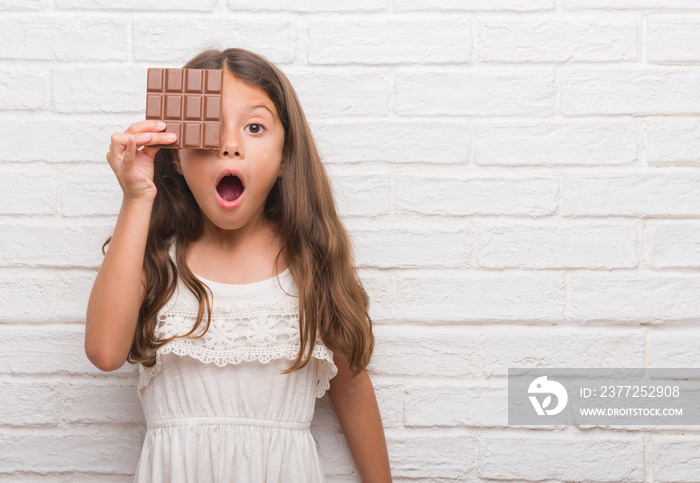 年轻的西班牙孩子在白色砖墙上吃巧克力，吓得一脸惊讶，