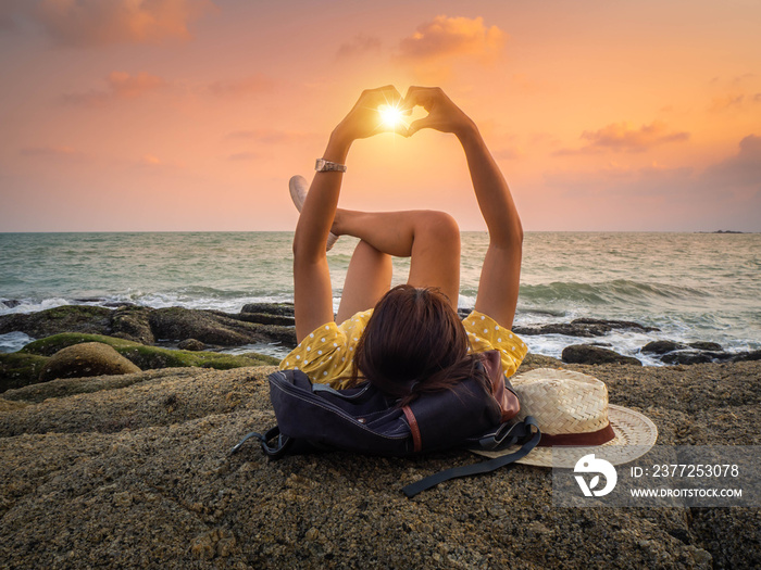 Hipster woman lying on the rock show the hand of heart in sunset time.