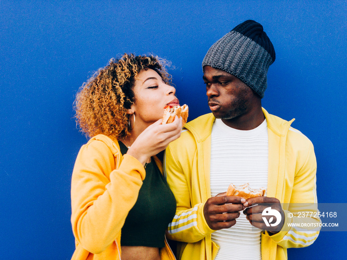 African man and latin woman eating hamburger together.