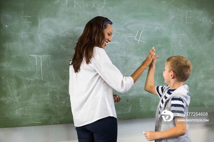 Happy teacher and school boy giving high five in classroom