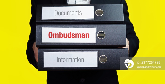 Ombudsman – finance/economics. Man carries a stack of 3 file folders. A folder has the label Ombudsm