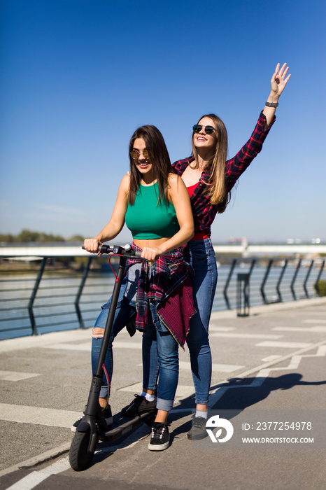 漂亮的年轻女性朋友在街上骑着电动滑板车