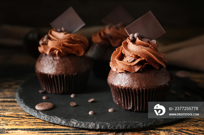 Slate plate with tasty chocolate cupcakes on wooden table