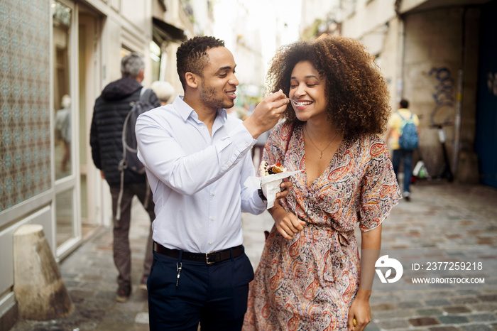 Loving boyfriend feeding food to girlfriend while walking on street in city