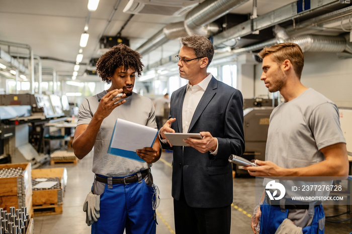 Young manual workers and their manager communicating while working on reports in industrial building