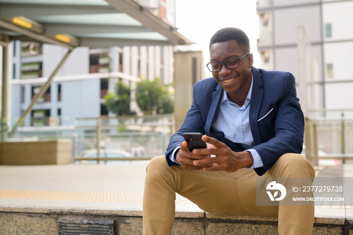 年轻快乐的非洲商人坐在地铁站外打电话