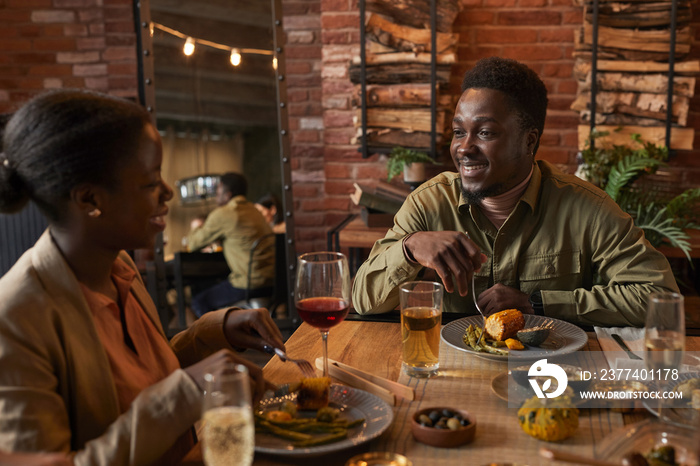Portrait of young African-American man smiling at girlfried while enjoying dinner party outdoors
