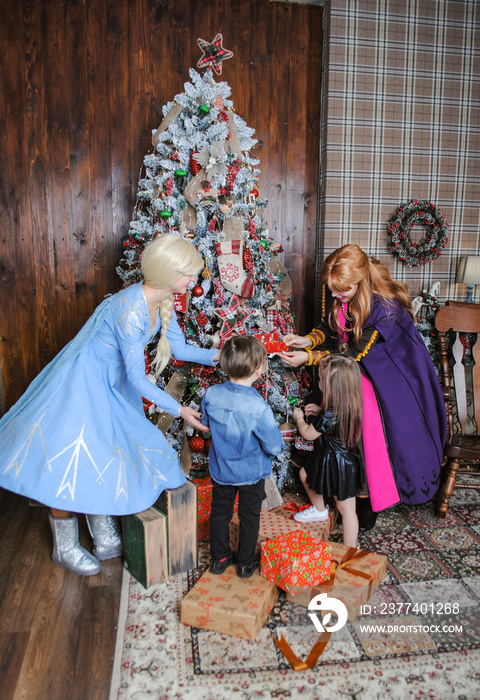 small children at home on the background of the christmas tree dress it up with Disney princesses fr