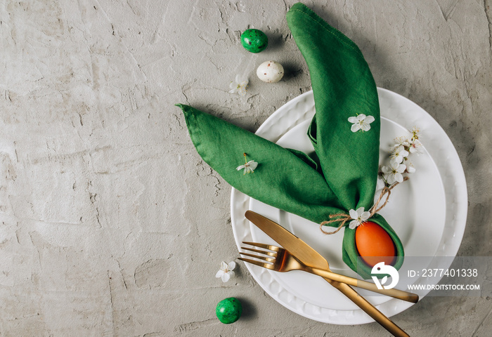 Easter table setting. Empty plates with green linen napkin and golden cutlery on concrete background