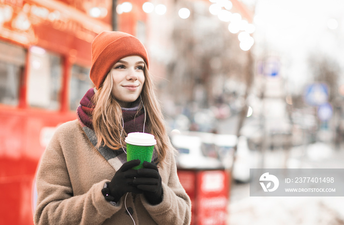 Winter street portrait of a cute girl in warm clothes on the street, standing with a cup of warm dri