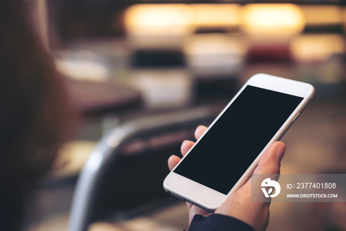 Mockup image of hand holding white mobile phone with blank black screen with blur background