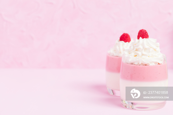 Raspberry panna cotta decorated with cream and ripe berry on pastel pink background.