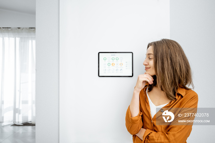 Portrait of a young and happy woman standing near touch screen panel for smart home control in the h