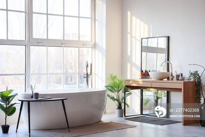 Interior of light bathroom with bathtub, table and mirror