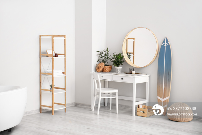 Interior of stylish bathroom with surfboard, table and mirror