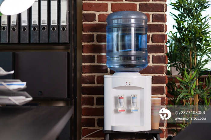 Close up of water dispenser used for refreshment in business office. Watercooler and bookshelf with 