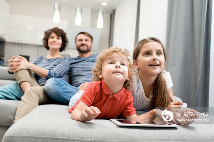 Portrait of happy family with two kids  watching TV together sitting on sofa in living room, focus o