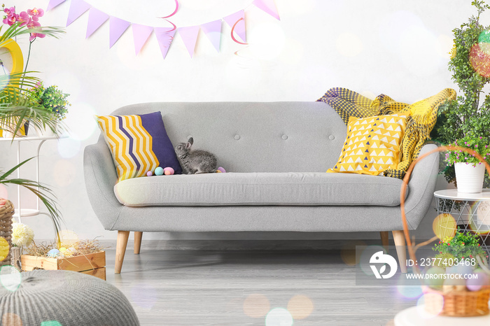 Cute rabbit and Easter eggs on grey sofa in room