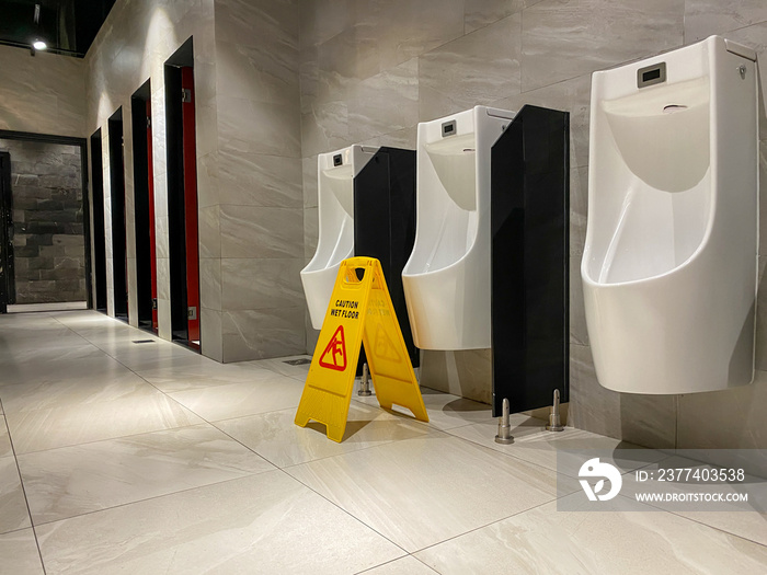 Wet floor sign near urinals area in public toilet during cleaning process