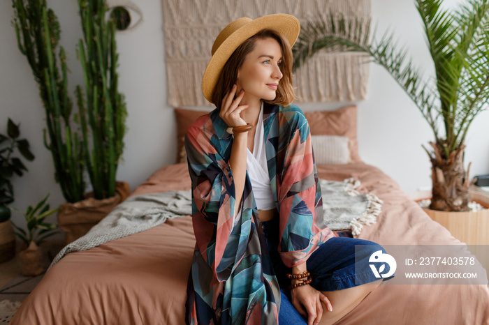 Happy woman in straw hat siting  in bohemian bedroom.