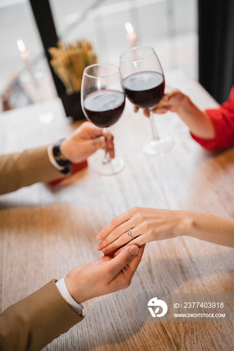 cropped view of woman with engagement ring on finger clinking glasses of wine with boyfriend on vale