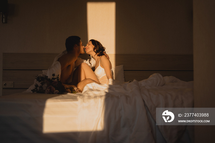 Couple kissing on bed in the morning. Graceful young lady with tanned skin gently kissing her sleepy