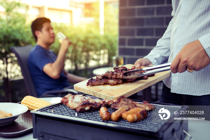 Asian men are pinching pork on a wooden cutting board and holding it to friends who are celebrating 