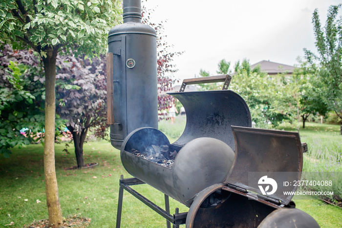 Smoker grill in home backyard, container with coal, smoke coming out of a smokestack, barbecue on gr